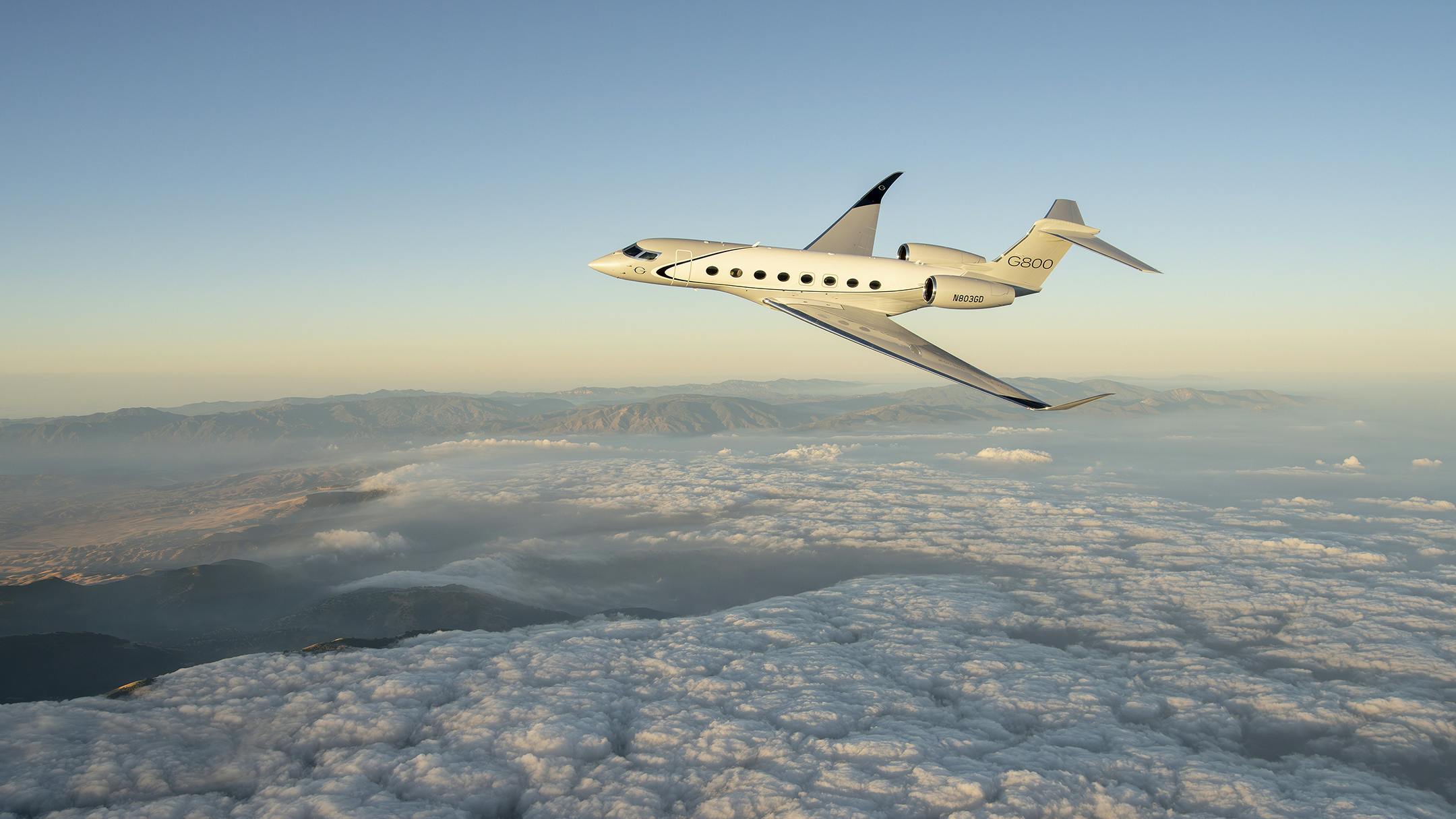 A cream-colored aircraft flying above a mountainous region and clouds