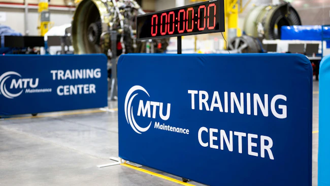 Two signs that read, 'MTU Maintenance Training Center' standing near a clock set at 00:00