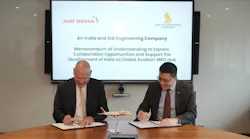 Two men wearing suits sitting at a table and signing pieces of paper, with text on a board behind them that reads: Air India and SIA Engineering Company Memorandum of Understanding to Explore Collaboration Opportunities and Support the Development of India as a Global Aviation MRO Hub