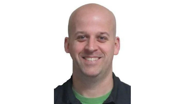 A close-up headshot of a man smiling at the camera