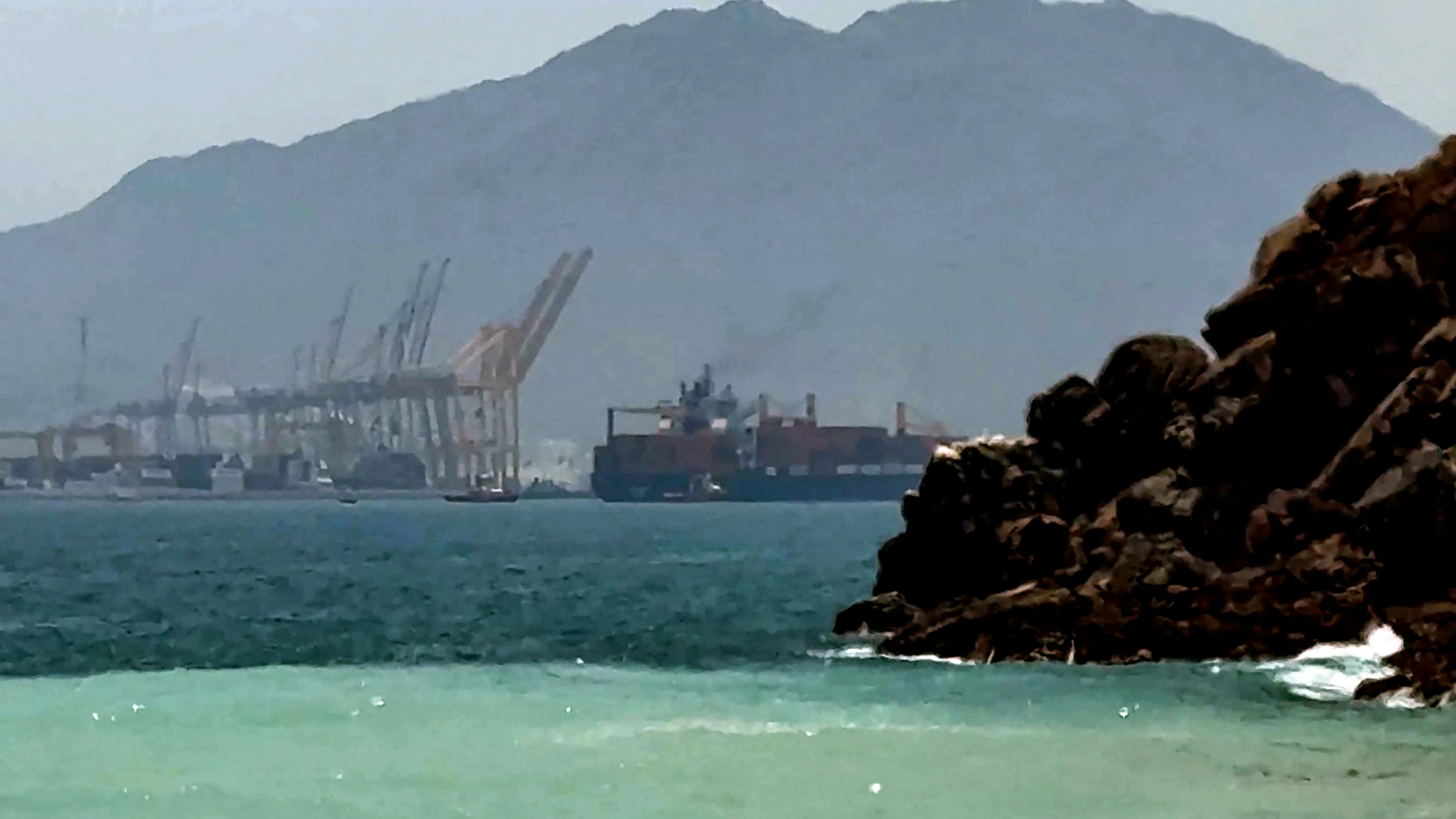 A photograph of mountain ranges near the sea, with industrial equipment in the background
