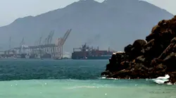 A photograph of mountain ranges near the sea, with industrial equipment in the background