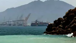 A photograph of mountain ranges near the sea, with industrial equipment in the background
