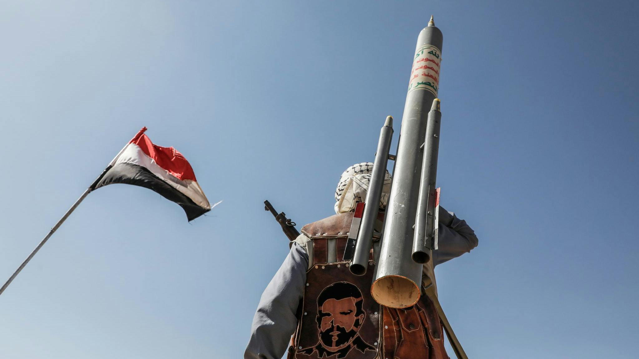 A photograph of a military soldier with a missile standing under a flag