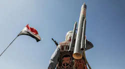 A photograph of a military soldier with a missile standing under a flag