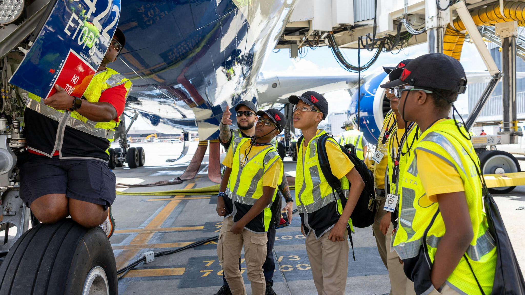 A group of young students in high-visibility vests looking under an airplane with a technician presenting from on the landing gear