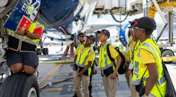A group of young students in high-visibility vests looking under an airplane with a technician presenting from on the landing gear