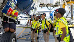 A group of young students in high-visibility vests looking under an airplane with a technician presenting from on the landing gear
