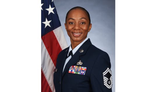 A woman wearing formal military dress smiling at the camera and standing in front of an American flag