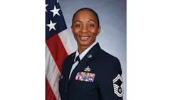 A woman wearing formal military dress smiling at the camera and standing in front of an American flag