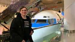 A man wearing a graphic tee and jacket standing in front of an airplane in a museum