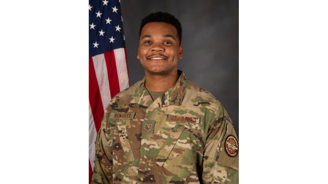 A man wearing military fatigues and standing in front of an American flag smiling at the camera in a professional headshot