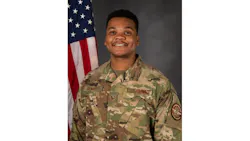 A man wearing military fatigues and standing in front of an American flag smiling at the camera in a professional headshot