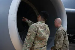 Two men wearing military fatigues looking closely at an aircraft engine, with one pointing inside
