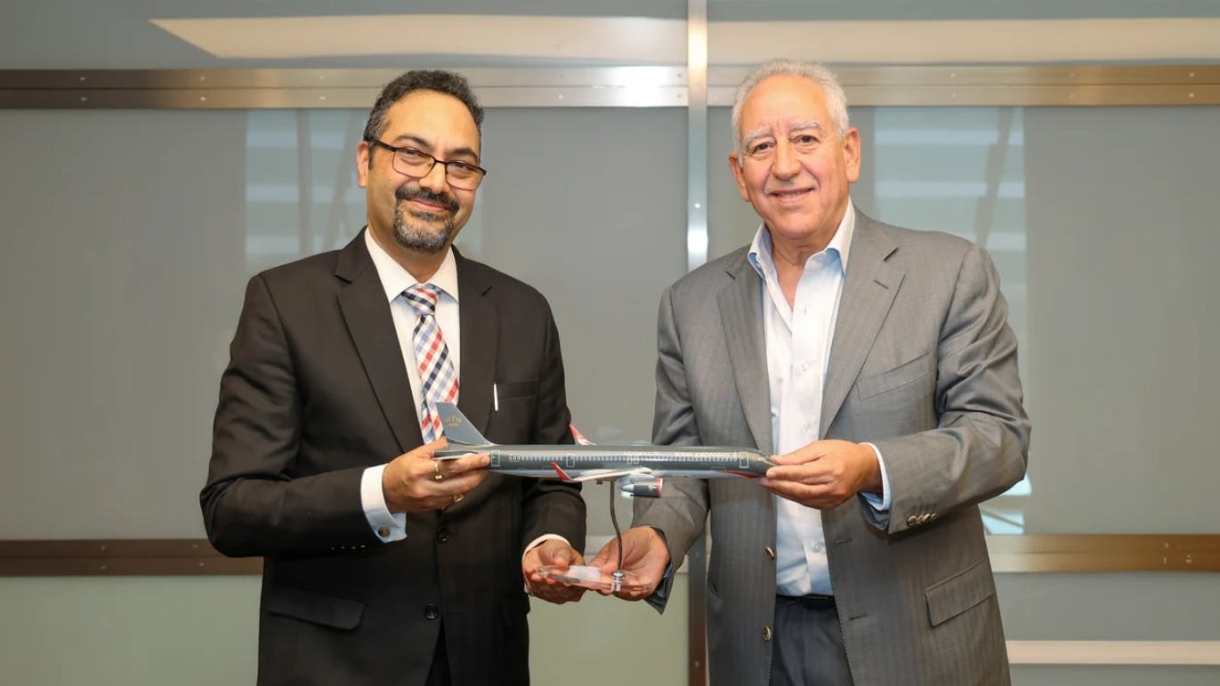 Two men wearing suits smiling at the camera while holding on to a model airplane