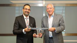Two men wearing suits smiling at the camera while holding on to a model airplane