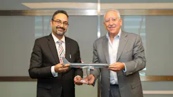 Two men wearing suits smiling at the camera while holding on to a model airplane
