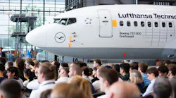 A large crowd of people standing inside an aircraft hangar with an airplane in the background labeled with text that reads: LUFTHANSA