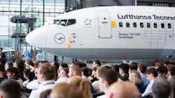 A large crowd of people standing inside an aircraft hangar with an airplane in the background labeled with text that reads: LUFTHANSA