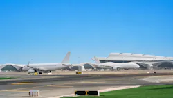 A long-distance photograph of an airfield with airplanes parked on it and a terminal in the background