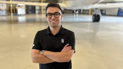 A man wearing glasses and a black polo crossing his arms and smiling at the camera while standing in front of an airplane
