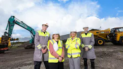 Two men and two women wearing white hard hats and high-visibility vests standing in front of a construction site