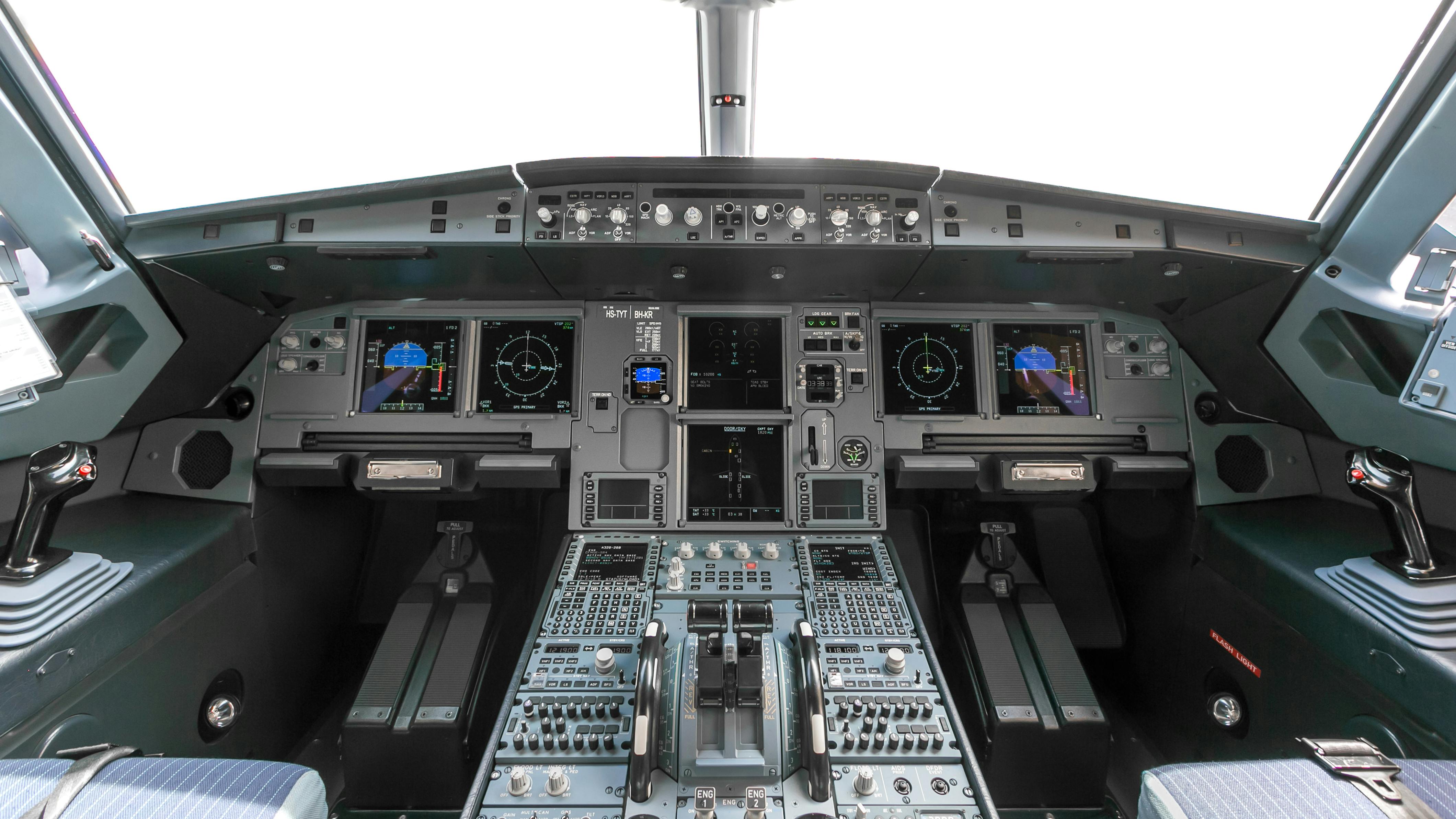 An avionics dashboard inside an airplane cockpit, with dials, buttons, switches and screens