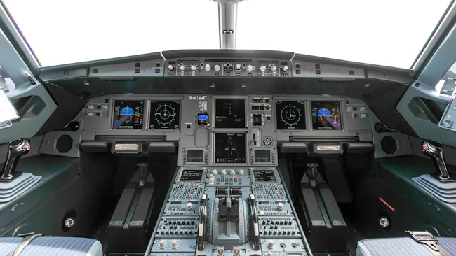 An avionics dashboard inside an airplane cockpit, with dials, buttons, switches and screens