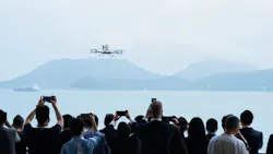 A large crowd of people watching and taking photos of an aircraft in the air over a body of water