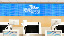 Self-service check-in kiosks and automated bag drop unit at Gerald R. Ford International Airport, with airport branding displayed on an overhead digital sign.