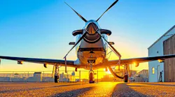 Single-engine turboprop aircraft parked nose-out on the tarmac at sunrise, with propeller blades crossed and a hangar visible in the background.