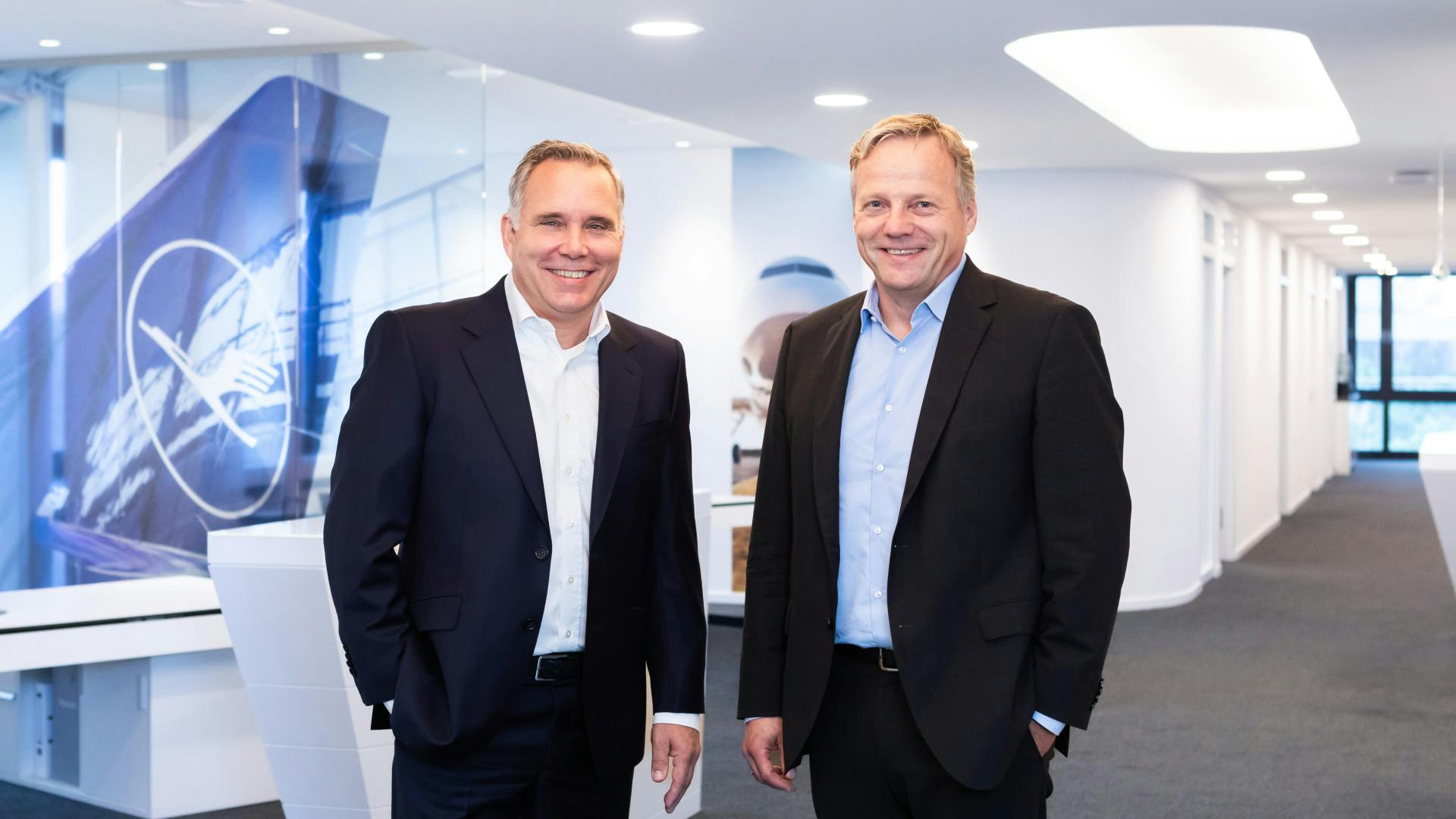 Two men wearing suits standing next to each other and smiling at the camera