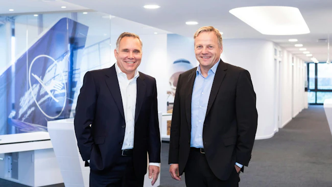 Two men wearing suits standing next to each other and smiling at the camera