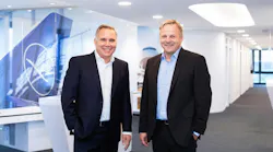 Two men wearing suits standing next to each other and smiling at the camera