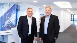 Two men wearing suits standing next to each other and smiling at the camera