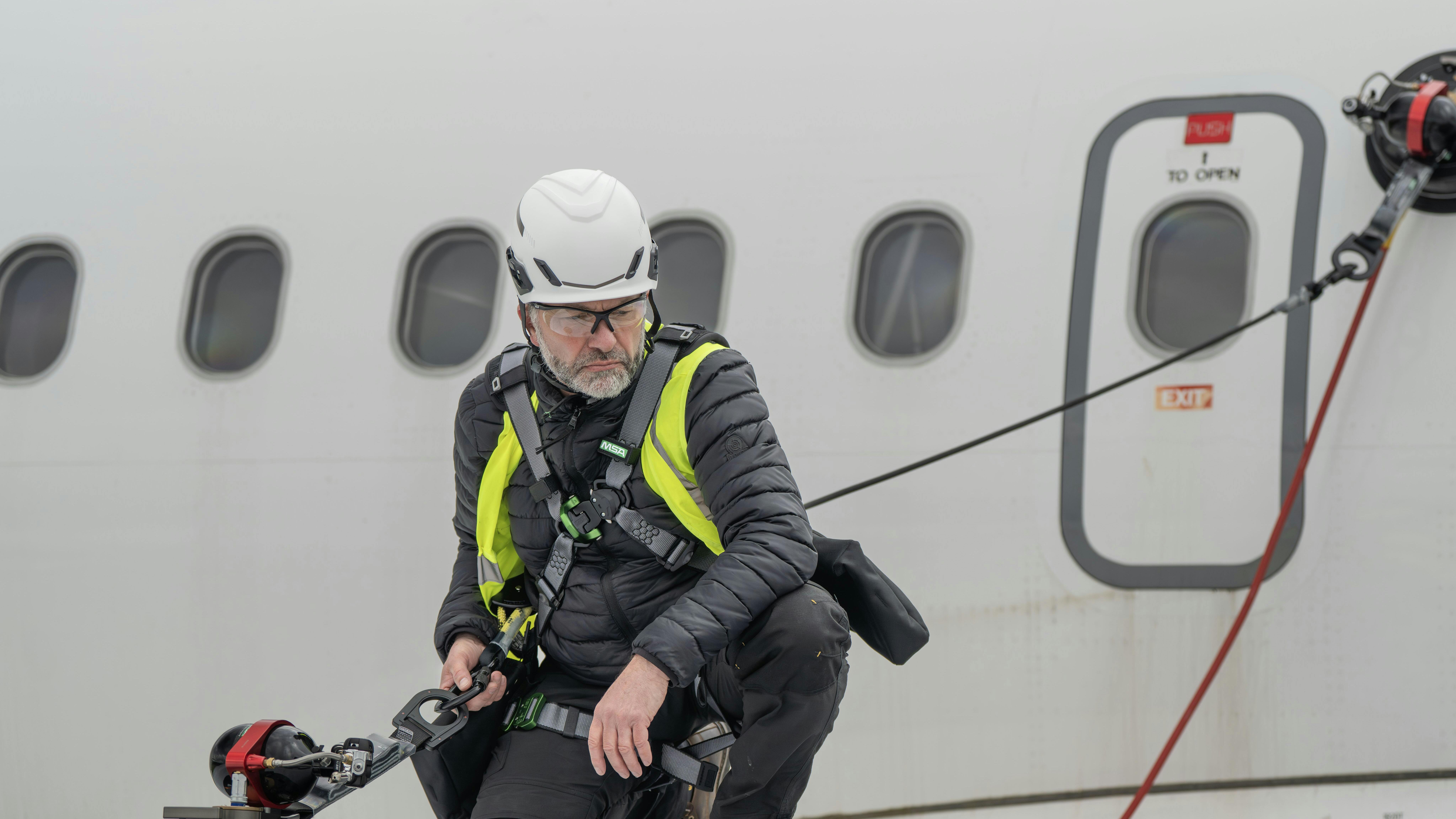 A technician standing on an airplane wing while tethered to an anchor suctioning to the plane's body
