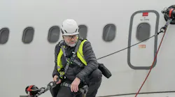 A technician standing on an airplane wing while tethered to an anchor suctioning to the plane's body