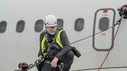A technician standing on an airplane wing while tethered to an anchor suctioning to the plane's body