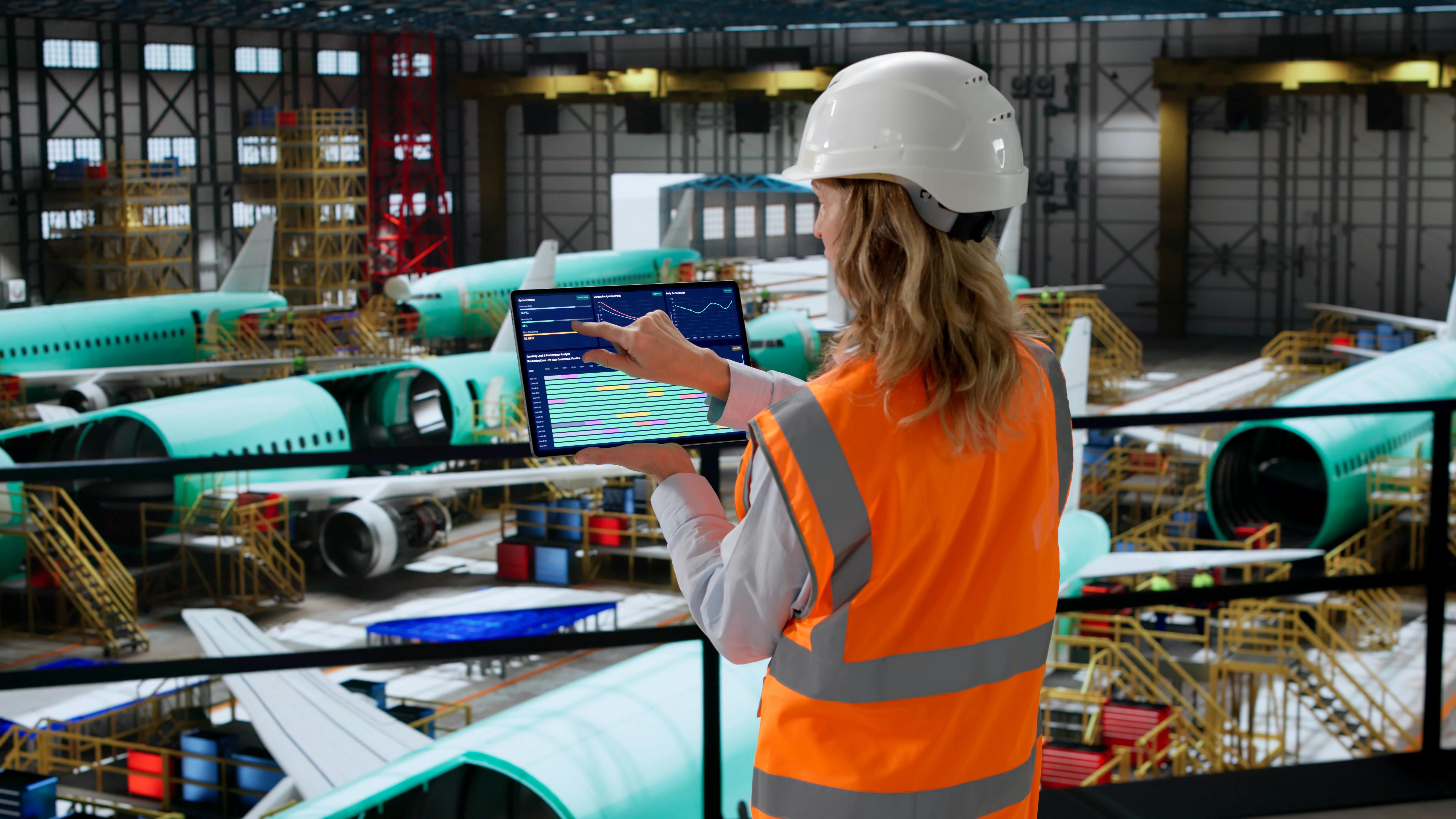 A technician standing in an aircraft hangar while touching a tablet screen, with airplanes parked in the background