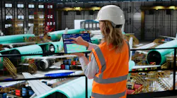 A technician standing in an aircraft hangar while touching a tablet screen, with airplanes parked in the background
