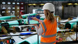 A technician standing in an aircraft hangar while touching a tablet screen, with airplanes parked in the background