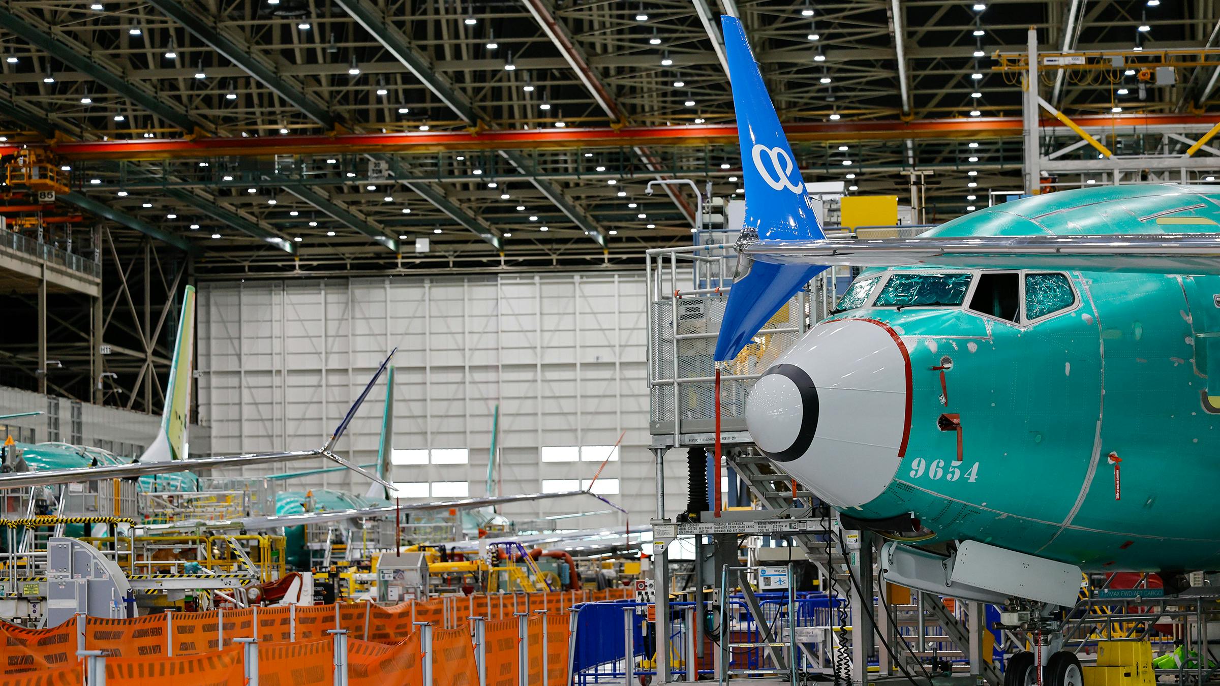 The front of a blue airplane in an airplane hangar with other airframe parts around it
