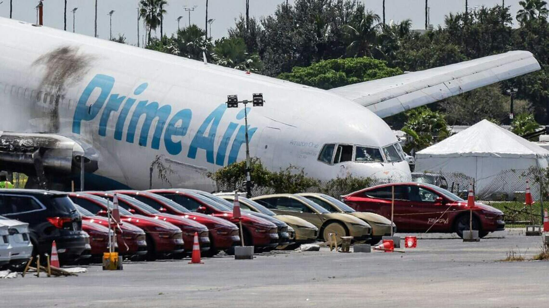 An airplane crashed into the ground nose-down by a line of cars, with text on the side that reads 'AMAZON'