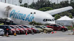 An airplane crashed into the ground nose-down by a line of cars, with text on the side that reads 'AMAZON'