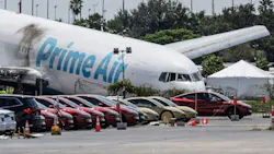 An airplane crashed into the ground nose-down by a line of cars, with text on the side that reads 'AMAZON'