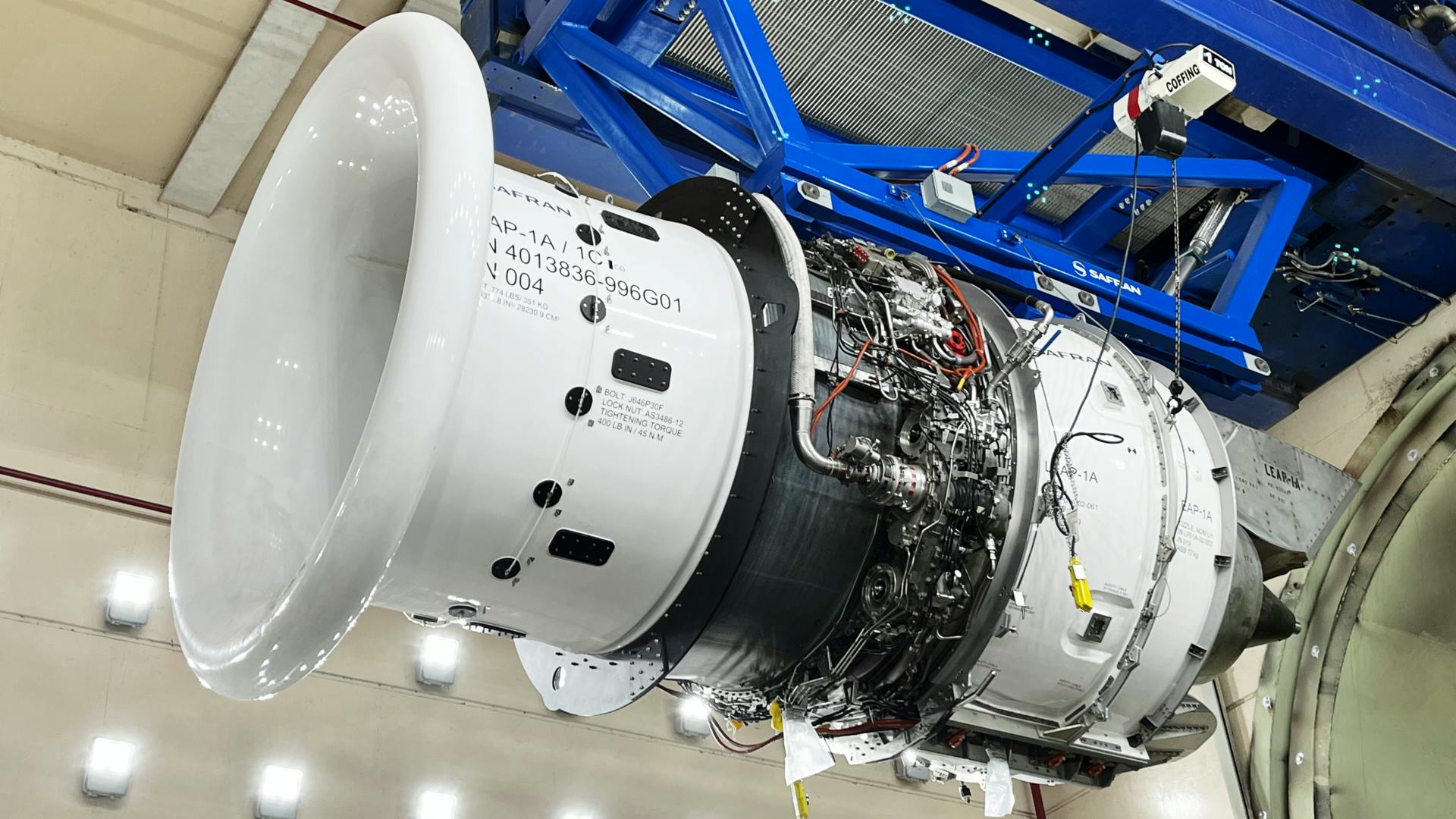 An aircraft engine being held up in the air by a piece of blue metal machinery