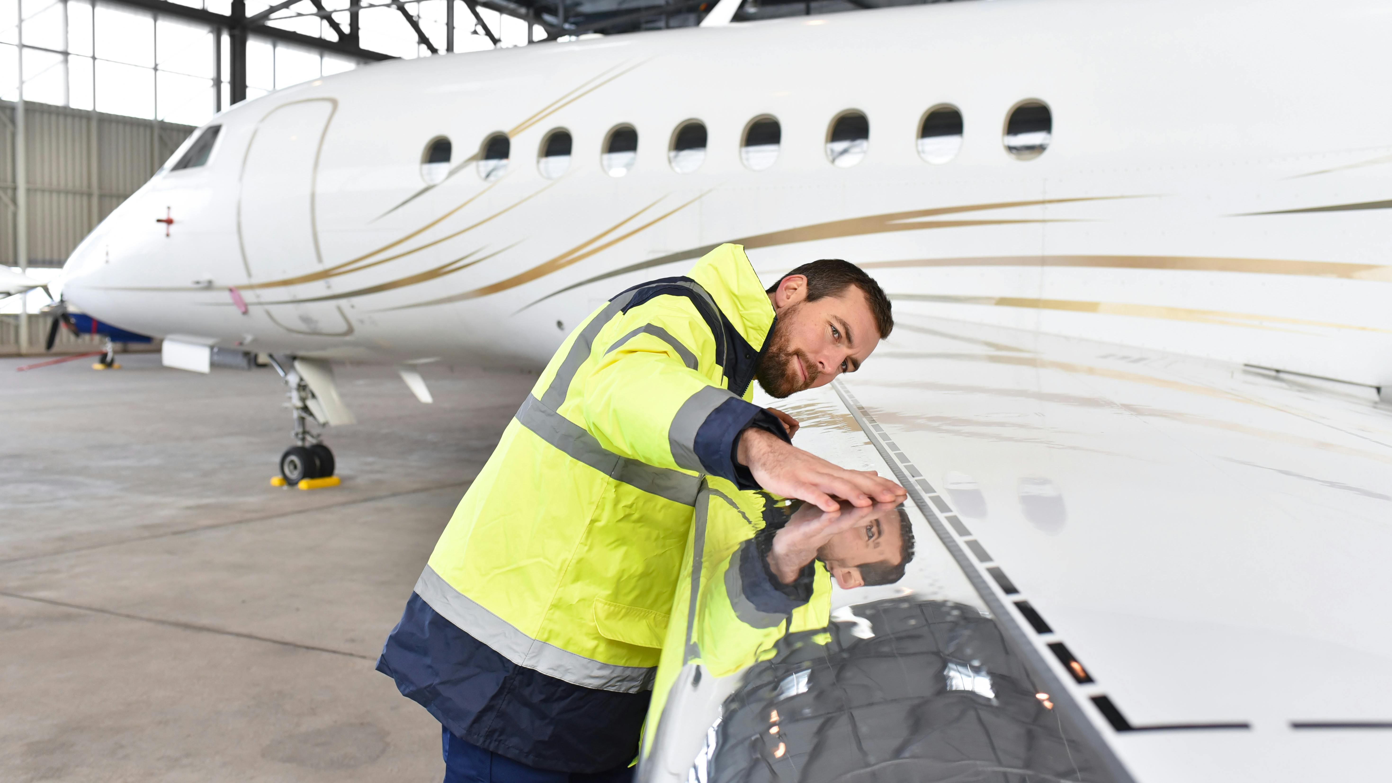A technician closely inspecting the wing of an airplane, putting his face close to the wing and stretching his arm out