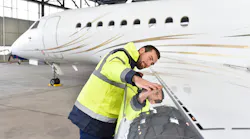 A technician closely inspecting the wing of an airplane, putting his face close to the wing and stretching his arm out