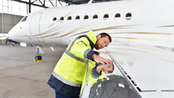 A technician closely inspecting the wing of an airplane, putting his face close to the wing and stretching his arm out