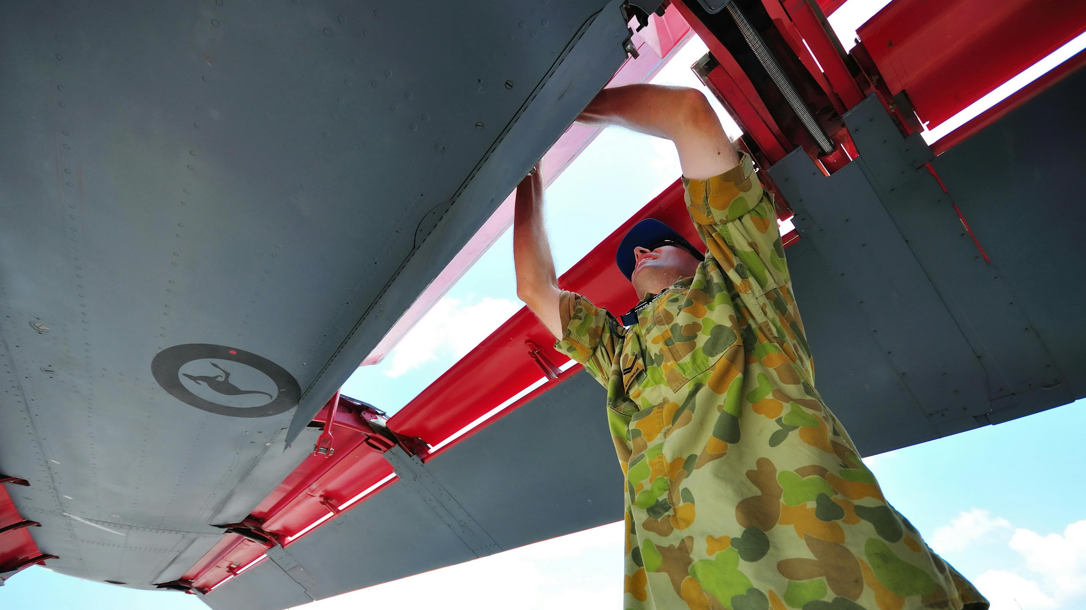 A technician wearing military fatigues standing under the wing of an airplane